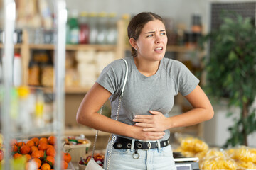 Young woman suffers from abdominal pain, feels pain in her stomach, while visiting a grocery supermarket