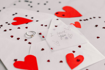 A handwritten note expresses love with the words I love you alongside a silver ring placed on a red paper heart, creating a romantic setting. Happy Valentine's Day