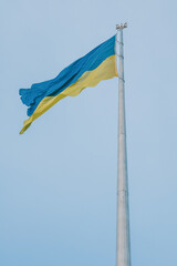 Ukrainian flag on a tall flagpole against a clear blue sky. National symbol representing patriotism and identity.