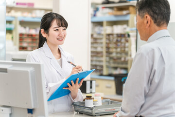 薬局のカウンターで患者をカウンセリング・ヒアリングする薬剤師の女性
