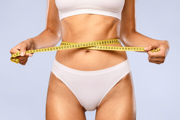 Cropped close up view of slim woman in white underwear measuring her waist with yellow tape...
