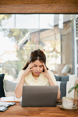 Young woman experiencing stress while working on a laptop in a cozy home office setting with natural light.