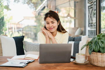 Obraz premium Smiling woman using a laptop at a stylish home office, surrounded by plants and books.