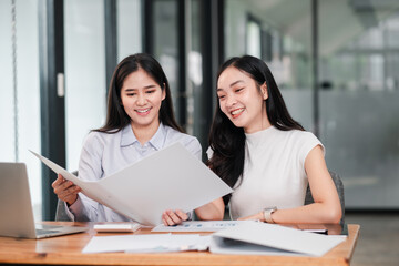 Two professional women reviewing documents in a modern office setting, showcasing teamwork and collaboration.