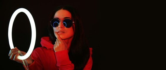Portrait of beautiful young woman holding neon lamp on dark background with space for text