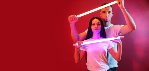 Portrait of young couple with neon lamps on red background with space for text