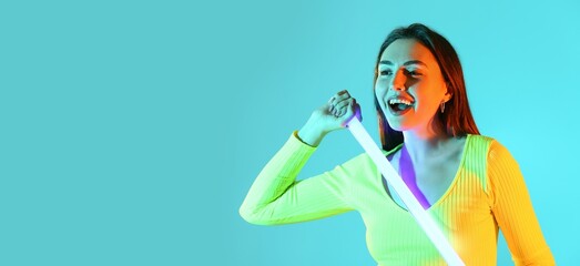 Toned portrait of beautiful young woman holding neon lamp on bright color background with space for text