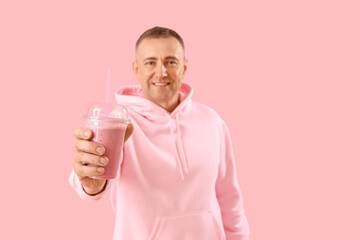 Mature man with glass of fruit smoothie on pink background