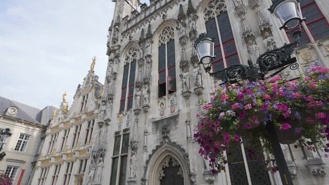 Establishing upward pan left to right of Bruges City Hall in De Burg Square with intricate Gothic architecture details and floral arrangement
