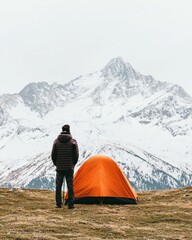 Fototapeta premium Exploring Nature's Beauty: A Solo Adventurer with an Orange Tent Against a Majestic Snowy Mountain View