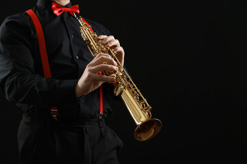Professional musician playing soprano saxophone on black background, closeup. Space for text