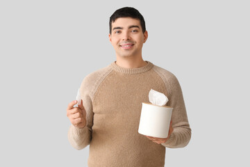 Young man with nasal drops and tissue box on light background