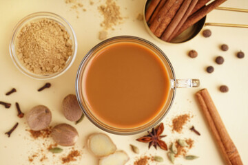 Glass cup of tasty masala tea with different spices on beige background, closeup