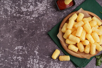 Wooden plate with tasty salty corn sticks and ketchup on grunge background