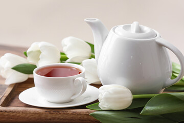 Tray with hot brewed pot of tea and tulips on table against blurred background
