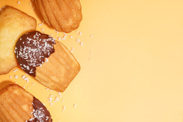 Delicious madeleines with chocolate and coconut flakes on yellow background