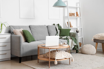 Modern interior of living room with grey sofa and laptop on table