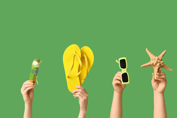 Female hands with stylish sunglasses, flip flops and starfish on green background