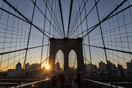 brooklyn bridge at sunrise (new york city landmark over east river to manhattan) travel tourism famous destination in usa america united states (suspension cables lamp light streetlight) people cross