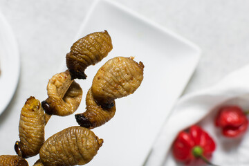 Overhead view of roasted sago worms, top view of palm worms on white background, roasted grub worms