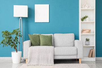 Cozy sofa, shelving unit, houseplant and floor lamp near blue wall in room