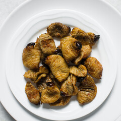 Overhead view of roasted sago worms on a white plate, top view of palm worms on marble background, roasted grub worms in a white dish