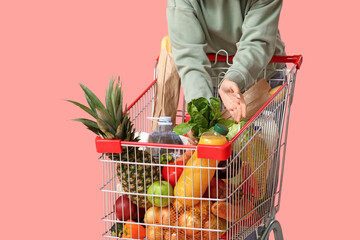 Beautiful young woman with full shopping cart on pink background, closeup © Pixel-Shot