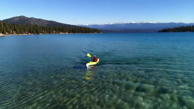 The aerial view captures a person kayaking on Lake Tahoe in California, USA. The individual paddles through the water, maneuvering the kayak along the lakes surface. 4K footage.