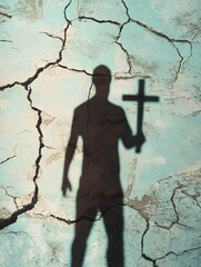 Silhouette of a man holding a cross cast as a shadow on cracked blue surface, minimalist religious symbolism and spiritual introspection concept