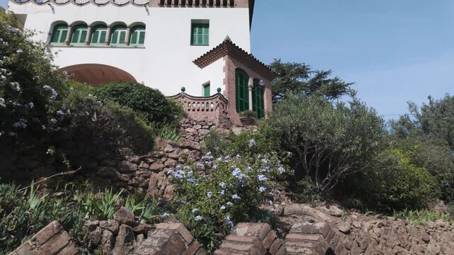 A charming view of Park G&uuml;ell's Casa Trias with vibrant greenery and rustic stonework, Barcelona
