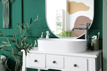 Sink with bath accessories on table and mirror near green wall in room