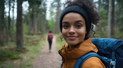 Biracial woman smiling in forest wearing orange jacket and blue backpack, celebrating National Public Lands Day in natural landscape environment