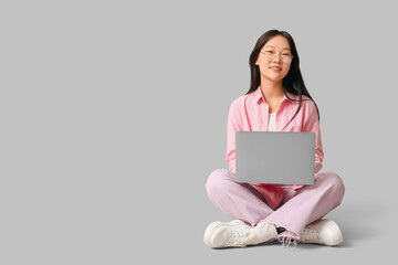 Naklejka premium Beautiful young Asian woman with modern laptop sitting on grey background