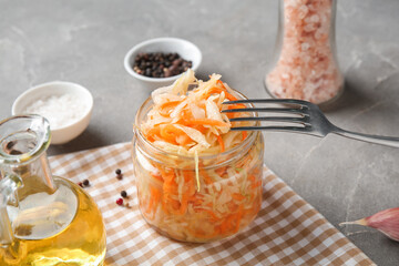 Glass jar with homemade sauerkraut, condiments and oil on grey background. Closeup