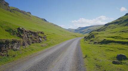 Naklejka premium A gravel road cutting through lush green hills in Iceland remote Westfjords, under a bright blue sky.