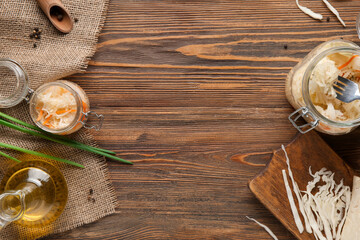 Glass jar with tasty sauerkraut and ingredients on wooden table. Top view
