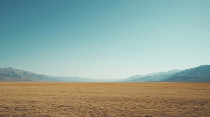 Obraz premium Expansive desert landscape with distant mountains under a clear blue sky, evoking tranquility and solitude