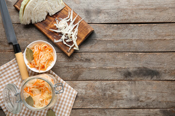 Glass jars and bowl with tasty sauerkraut and cabbage on wooden background. Top view