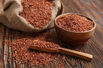 Bowl and sack with raw brown rice and scoop on wooden background