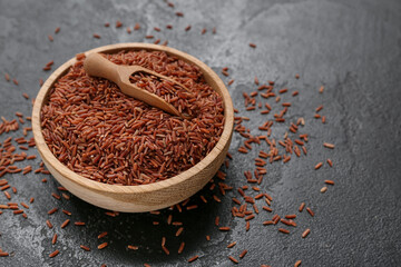 Wooden bowl with raw brown rice and scoop on black grunge background