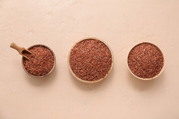 Wooden bowls with raw brown rice and scoop on beige background