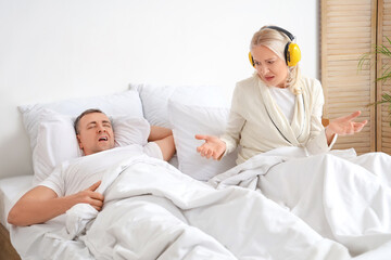 Obraz premium Mature woman with hearing protectors cannot sleep because of her husband's snoring in bedroom