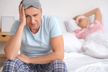 Annoyed mature man and his snoring wife in bedroom