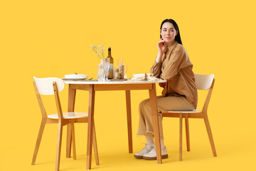 Young woman at restaurant table on yellow background