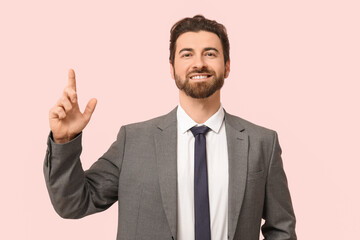 Young businessman pointing up on pink background