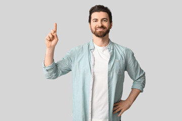 Young man pointing up on light background