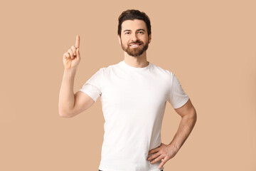 Young man pointing up on beige background