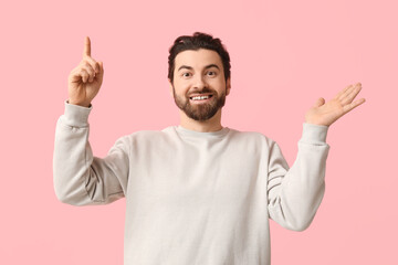 Young man pointing up on pink background