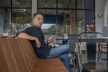 Man Sitting And Holding A Phone, Looking To The Side With Focus, Surrounded By Plants In A Relaxed, Calm, Casual Environment.