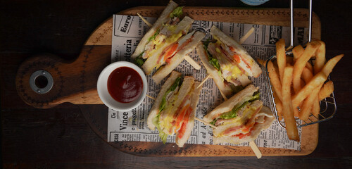 Top View of Club Sandwich with Lettuce, Tomato, and Chicken Served with French Fries and Ketchup on Wooden Board  